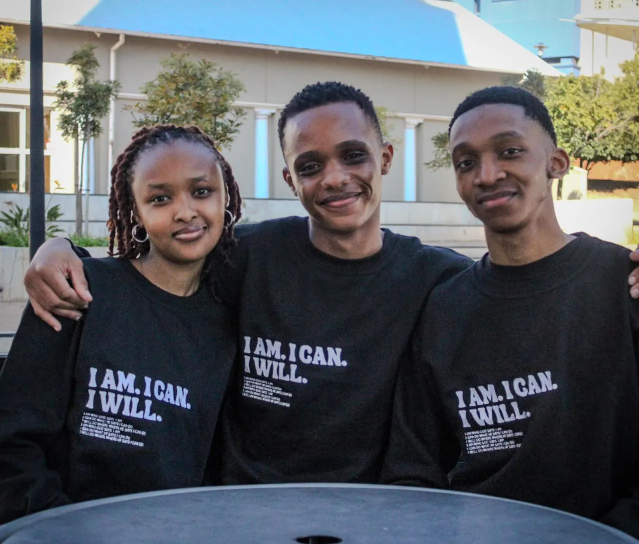 Three friends arm in arm wearing "I Am. I Can. I Will." sweaters